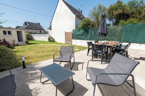 An outdoor patio with a table and chairs, a green fence, and a house in the background. - Charming house 2 minutes from the beaches, by Groom* (Ploemeur)