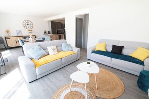 Un salon moderne avec deux canapés gris, une table à manger et une cuisine en arrière-plan.