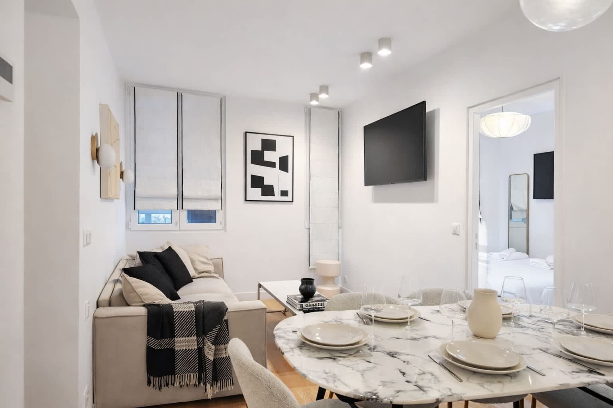 A modern living room with a sofa, a dining table set for four, and a TV mounted on the wall.