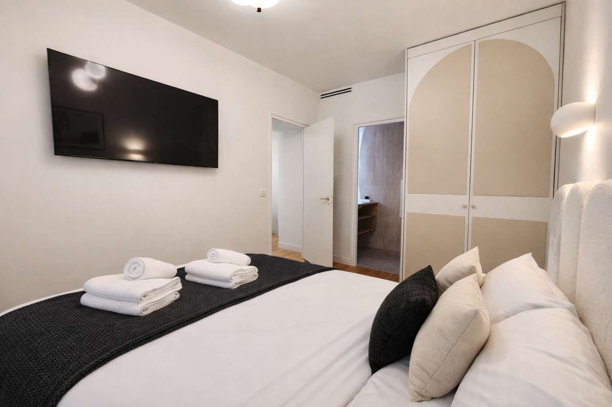 A hotel room with a bed, a flat-screen TV, a wardrobe, and a bathroom visible through an open door.