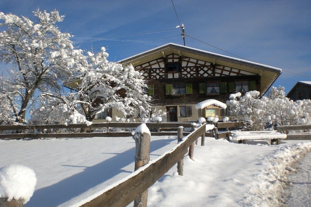 A traditional building with a gabled roof, surrounded by snow-covered trees and a wooden fence.