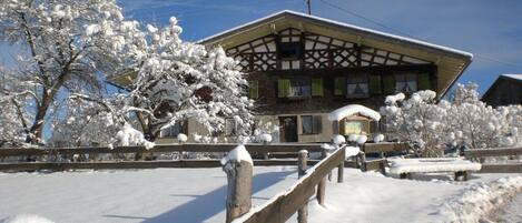 A traditional building with a gabled roof, surrounded by snow-covered trees and a wooden fence.