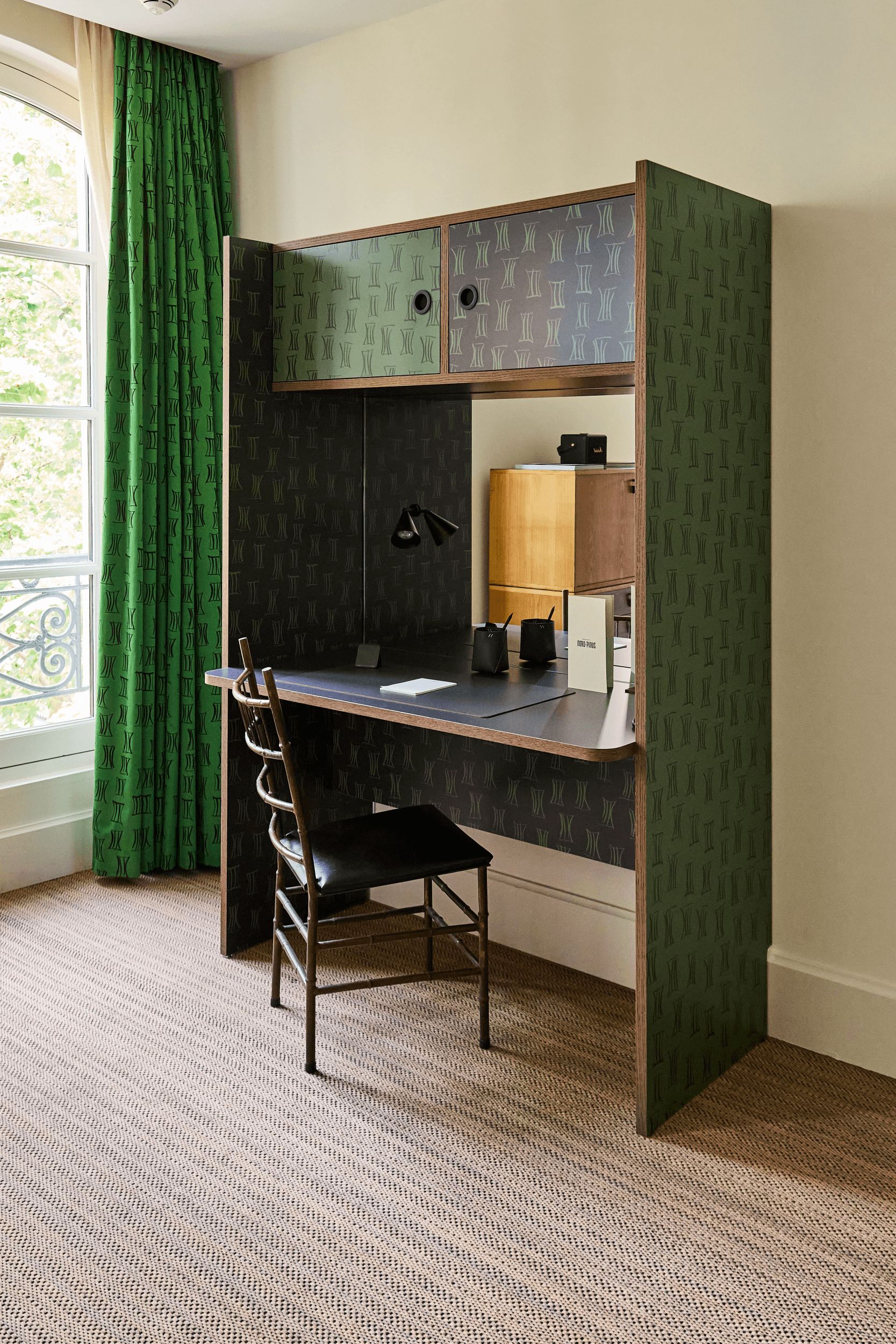 A room with a desk, chair, and a window with green curtains.