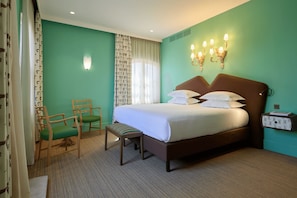 A hotel room with a large bed, a chair, a bench, and a nightstand with a lamp. - Grand Hôtel Nord-Pinus  (Arles)