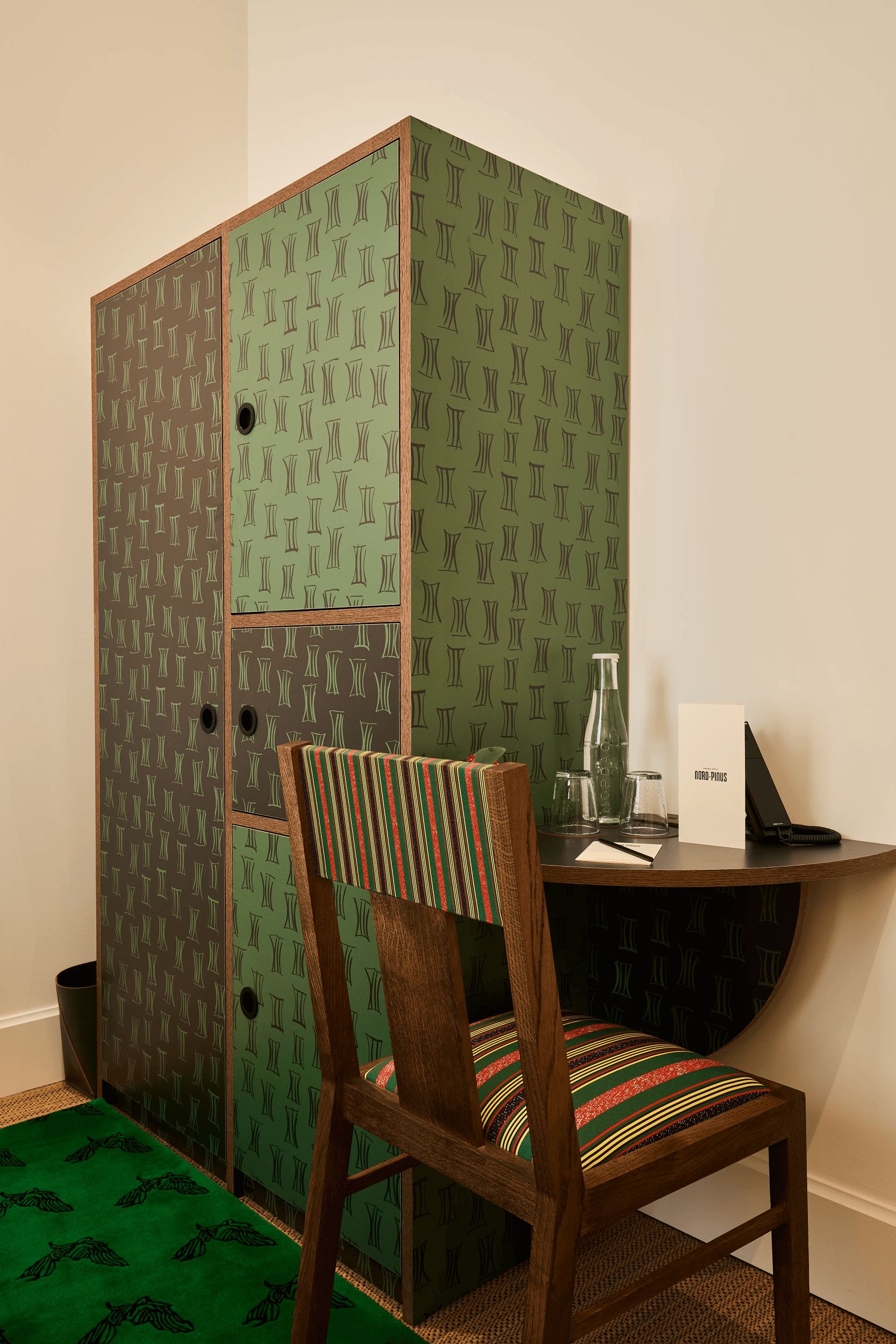 A room with a wooden chair, a desk with a computer, and a cabinet with patterned wallpaper.