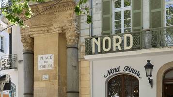 Un edificio con un letrero que dice 'NORD' y 'Nord Pinus', indicando un restaurante o cafetería. Hay mesas y sillas al aire libre, lo que sugiere un área de estar para clientes.