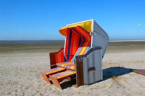 Une chaise de plage avec un coussin à rayures et le chiffre « 97 » inscrit dessus, placée sur une plage de sable fin sous un ciel dégagé.