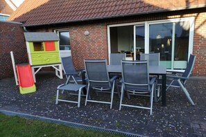 Eine Terrassengruppe mit Backsteinmauer, einem Spielhäuschen und einem Tisch mit Stühlen.