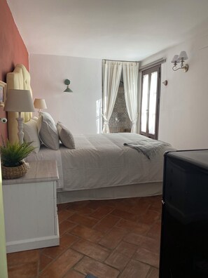 A bedroom with a bed, bedside lamps, a potted plant, a window with curtains, and a television. - Boutique-Eros House (Carmona)