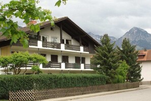 Ein zweistöckiges Gebäude mit Balkonen, umgeben von Grün und Bergen im Hintergrund.