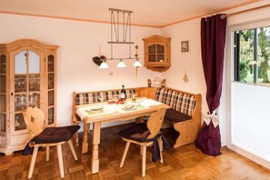 A dining area with a wooden table, chairs, and a bench. There is a cabinet with glass doors, a hanging light fixture, and a window with curtains. - Holiday apartment with 2 bedrooms (Fischen)
