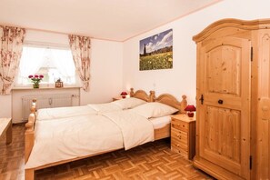 A bedroom with a double bed, wooden wardrobe, and a window with curtains. - Holiday apartment with 2 bedrooms (Fischen)