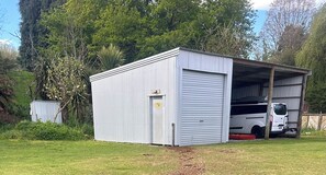A single-story metal building with a closed garage door, a small attached shed, and a white van parked inside.