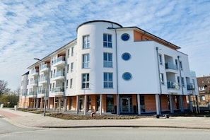 Ein mehrstöckiges Wohngebäude mit Balkonen, einem zentralen Eingang und blauem Himmel.