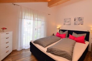 Ein Schlafzimmer mit Doppelbett, Schminktisch, einem Fenster mit transparenten Vorhängen und Wandlampen.