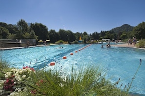 A swimming pool with multiple lanes, surrounded by greenery and a clear sky. - Holiday apartment with 1 bedroom (Fischen)