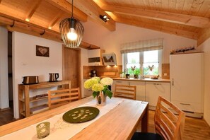A wooden dining table with chairs, a vase with flowers, and a hanging light fixture in a kitchen with wooden beams and white cabinets. - Holiday apartment with 1 bedroom (Fischen)