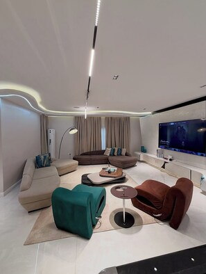 Un saló modern amb un televisor de pantalla plana gran, un sofà marró, un pouf color turquesa i una taula de centre.