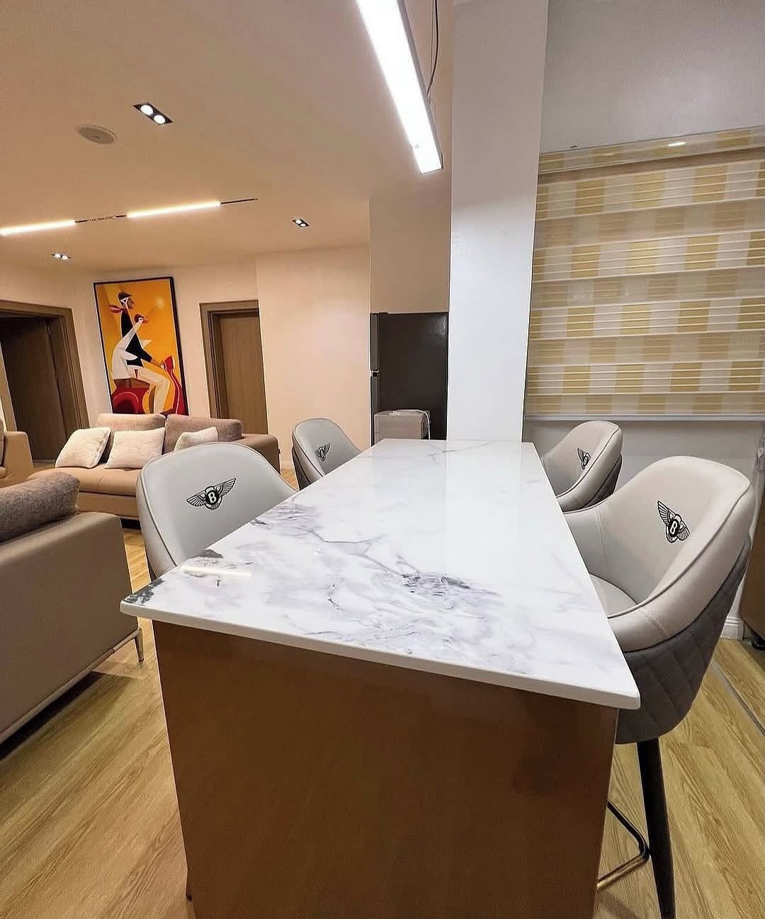 Una sala de estar moderna con una mesa de comedor de mármol, sillas de cuero, un sofá y un cuadro abstracto grande en la pared.