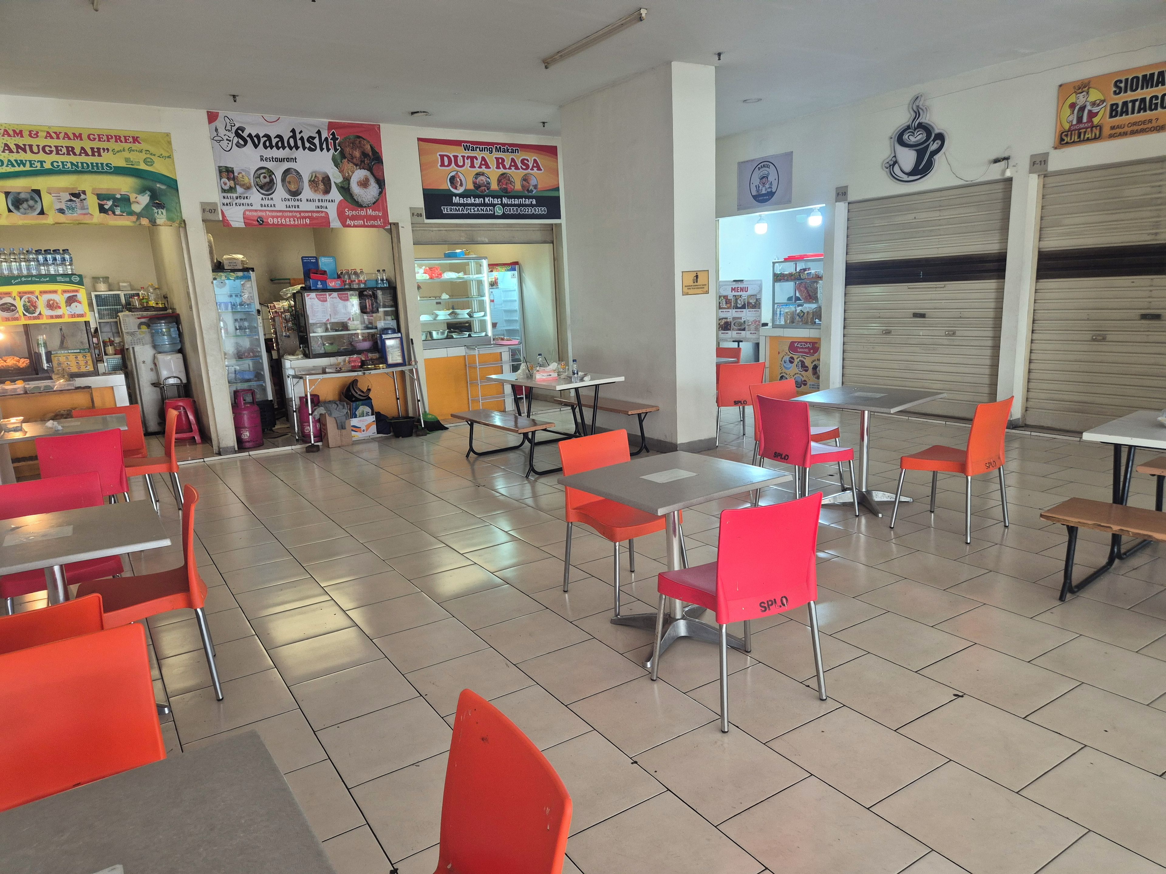 Interno di un ristorante con sedie e tavoli rossi, e un bancone con prodotti alimentari.