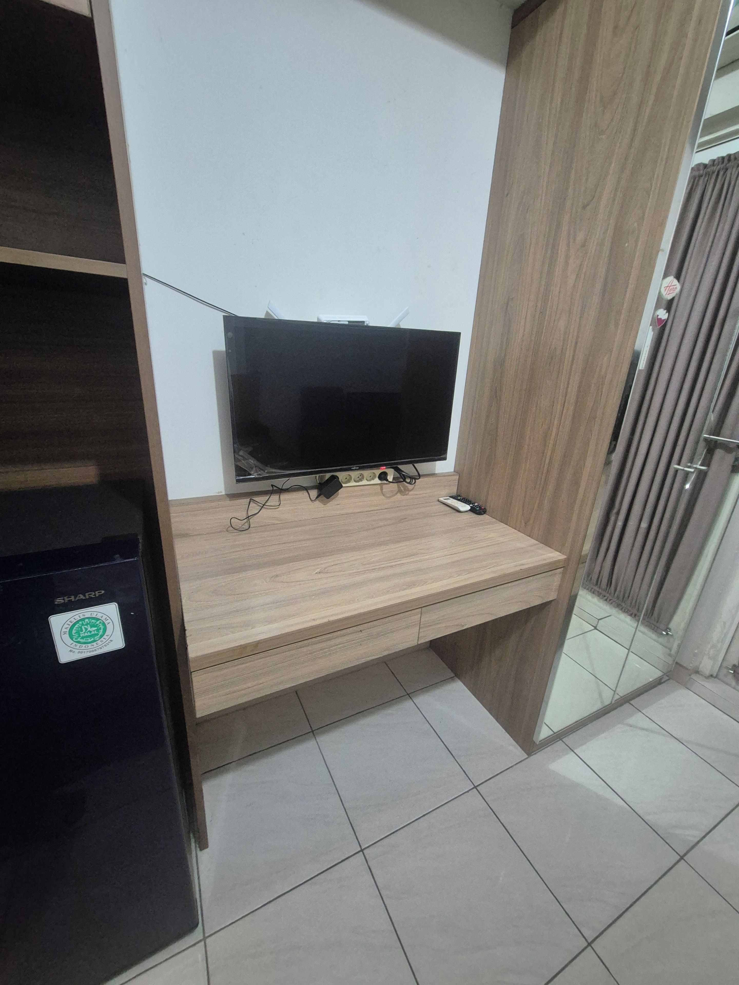 Una habitación con un escritorio de madera, televisor y refrigerador Sharp negro.