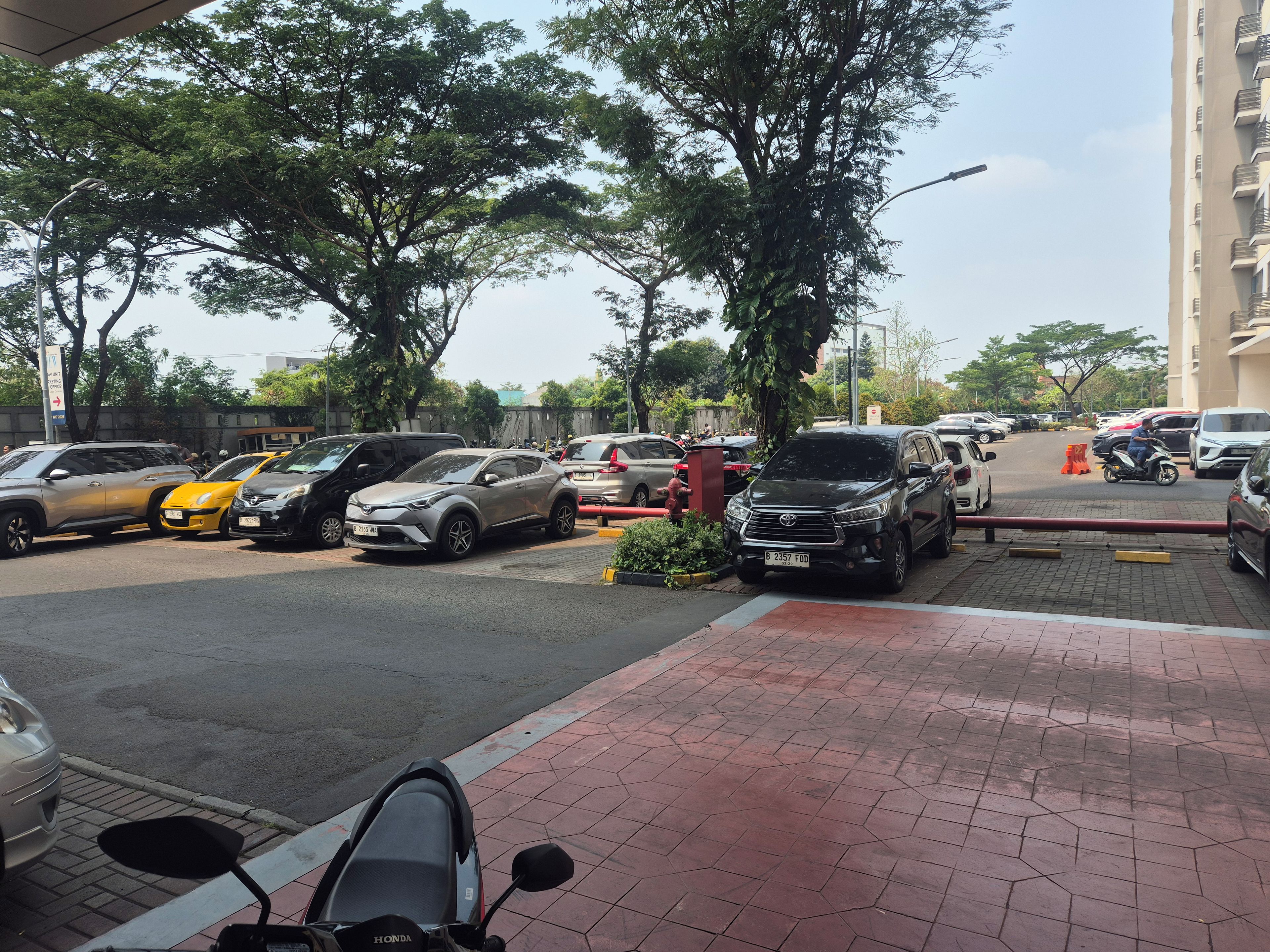 Um estacionamento com diversos veículos, incluindo carros e motocicletas, e uma área de passagem para pedestres.