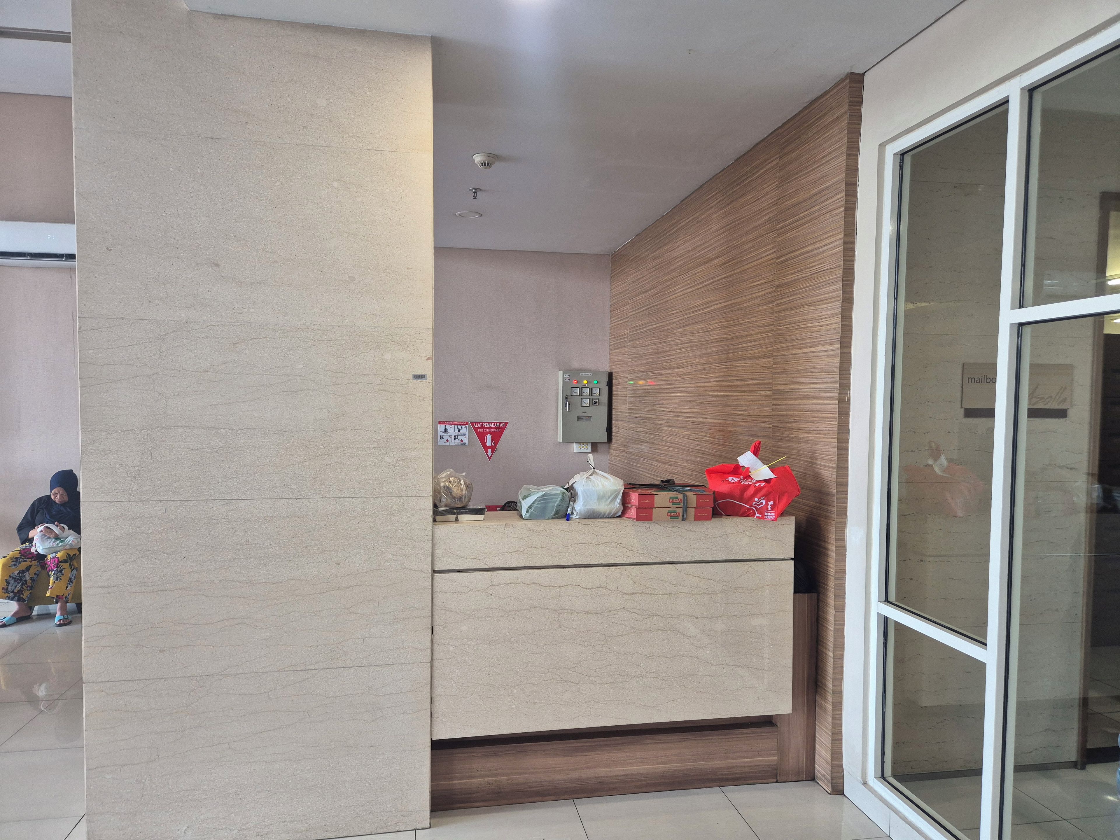 Un mostrador de recepción con un panel de pared de madera, un detector de incendios y una puerta de cristal con buzón.