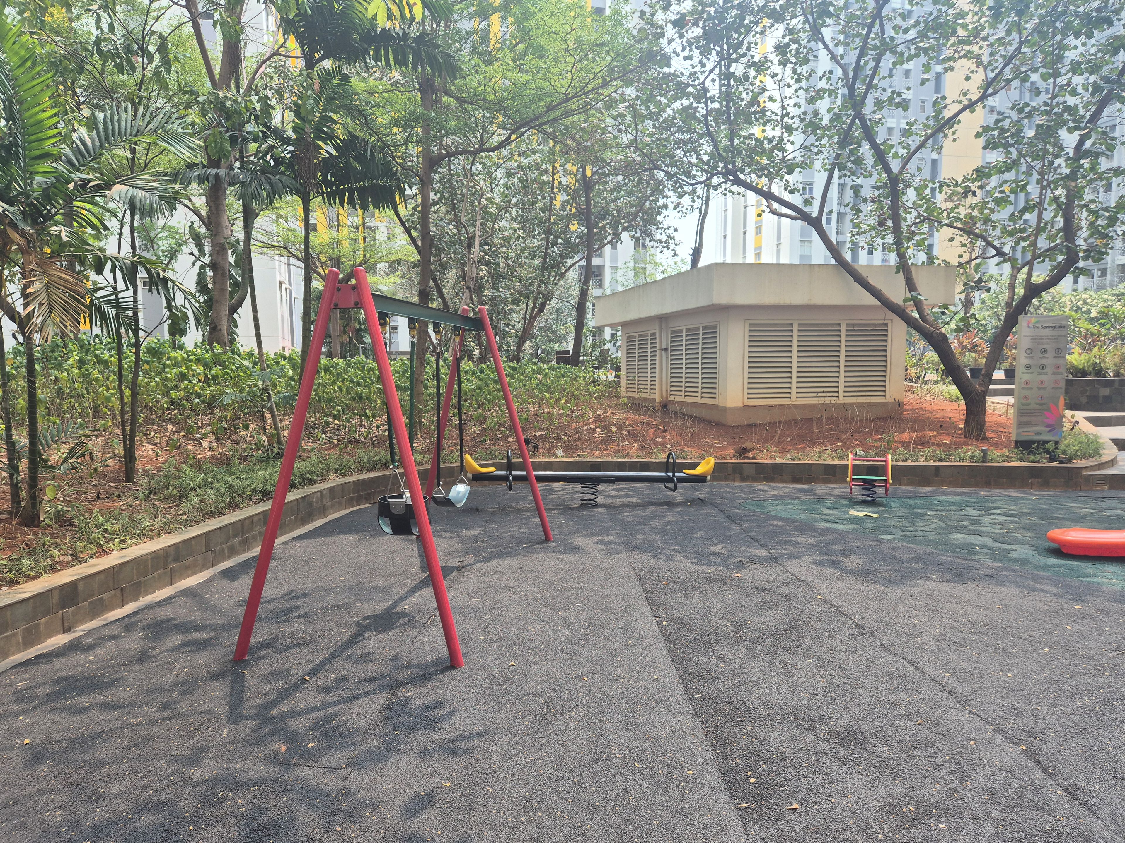 A playground with swings and a slide, surrounded by trees and a building.