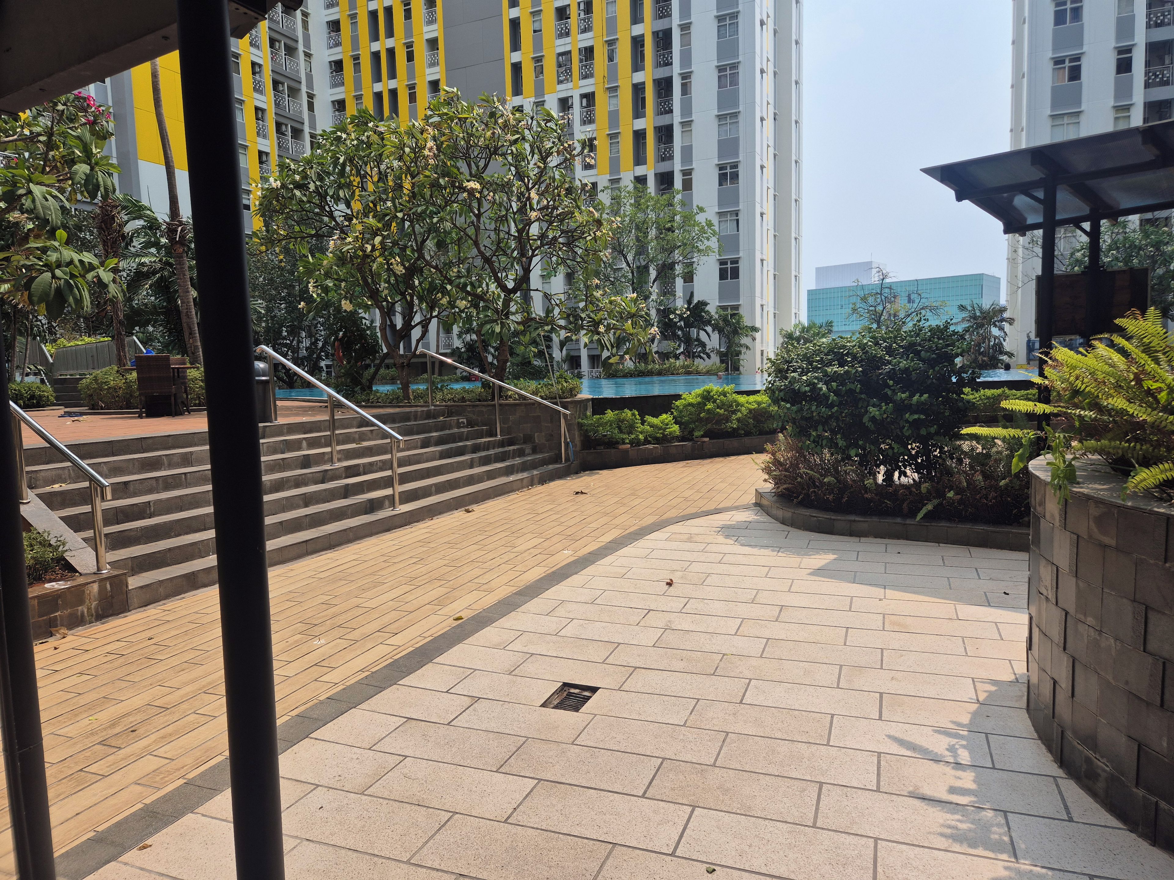 Un'area esterna pavimentata con gradini che conducono all'ingresso di un edificio, immersa nel verde e con un edificio moderno caratterizzato da tocchi gialli.