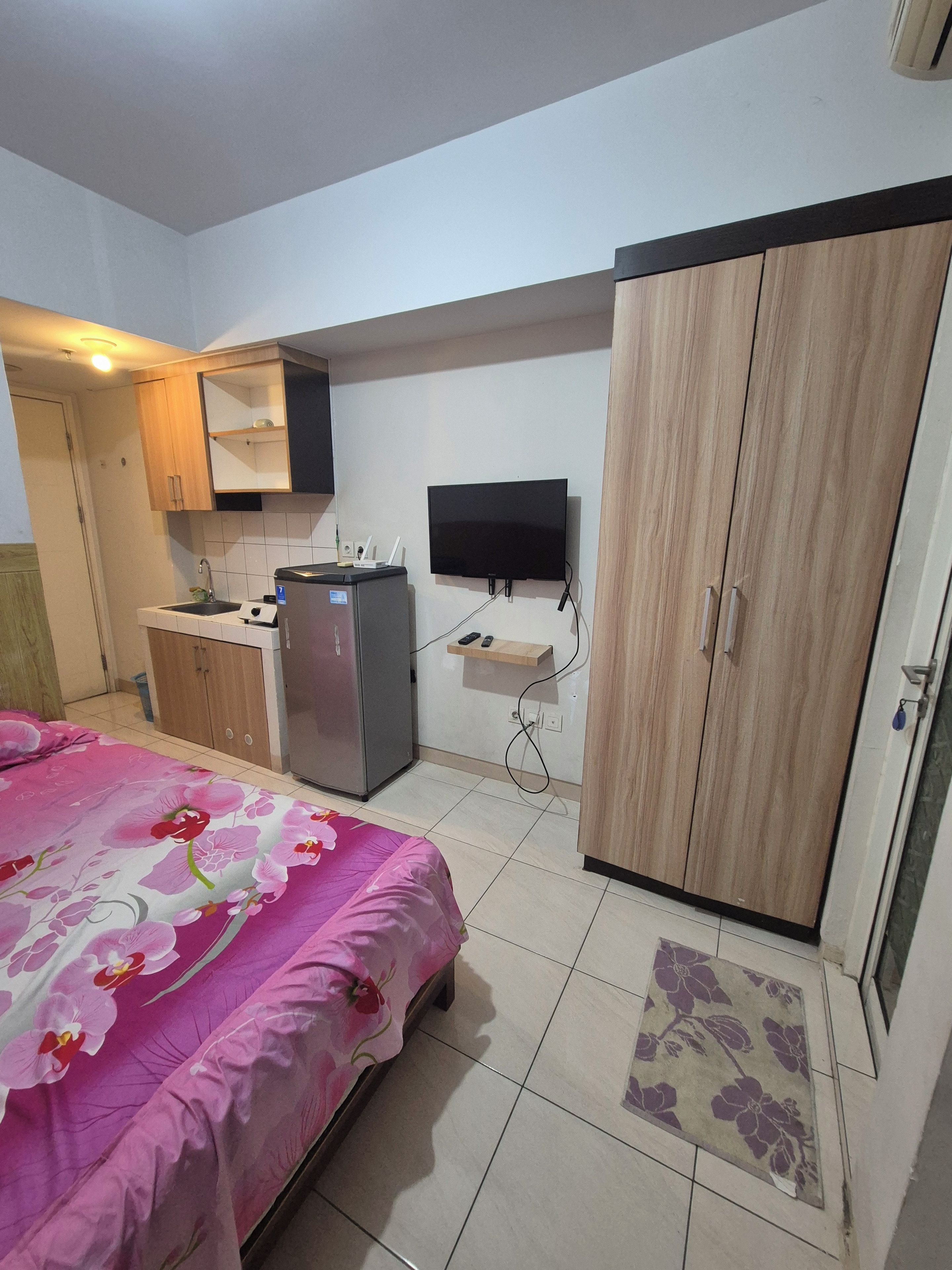 Un dormitorio con cama, armario, televisor y kitchenette.