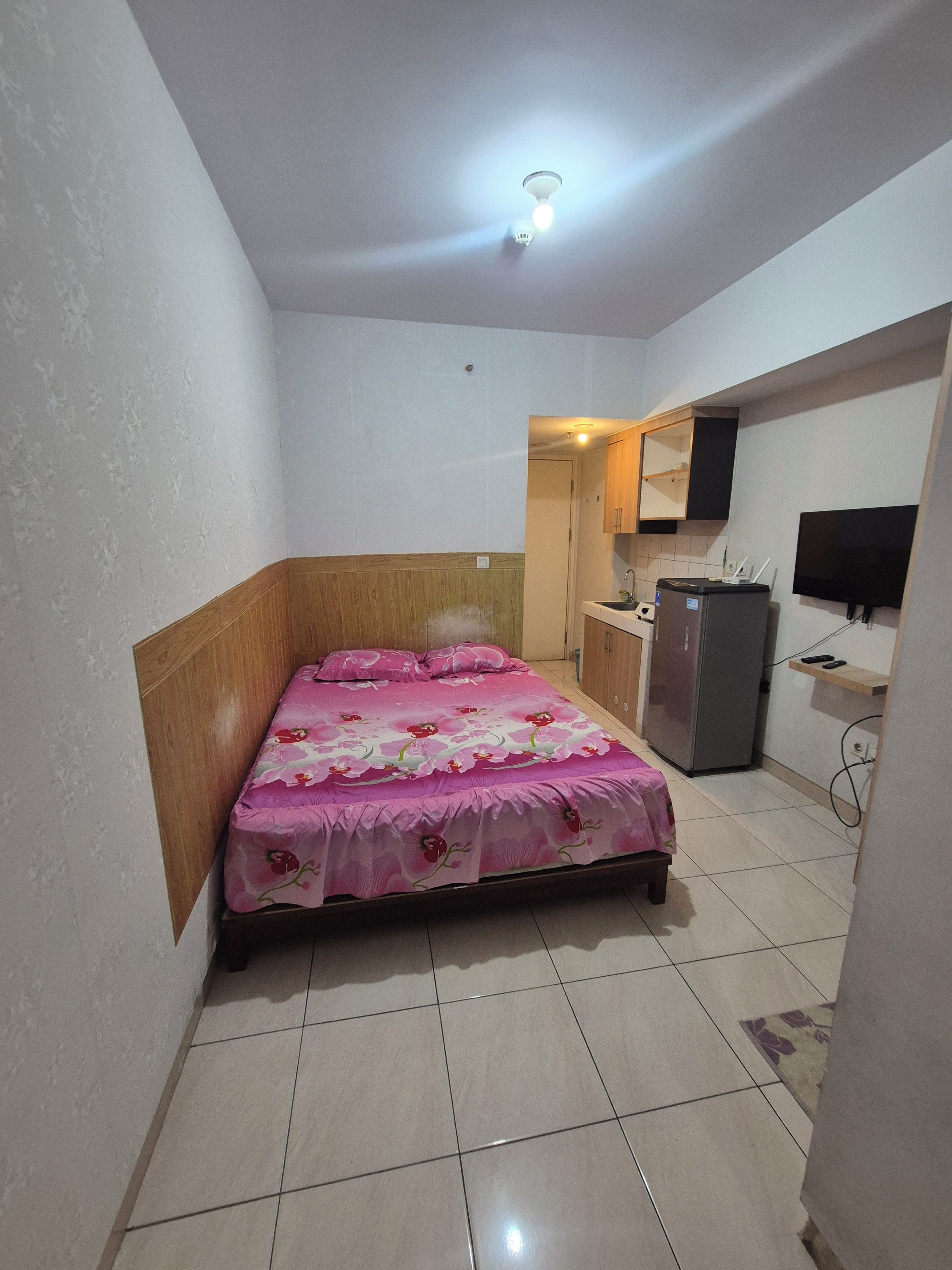 Un dormitorio con una cama, una kitchenette pequeña y un televisor.