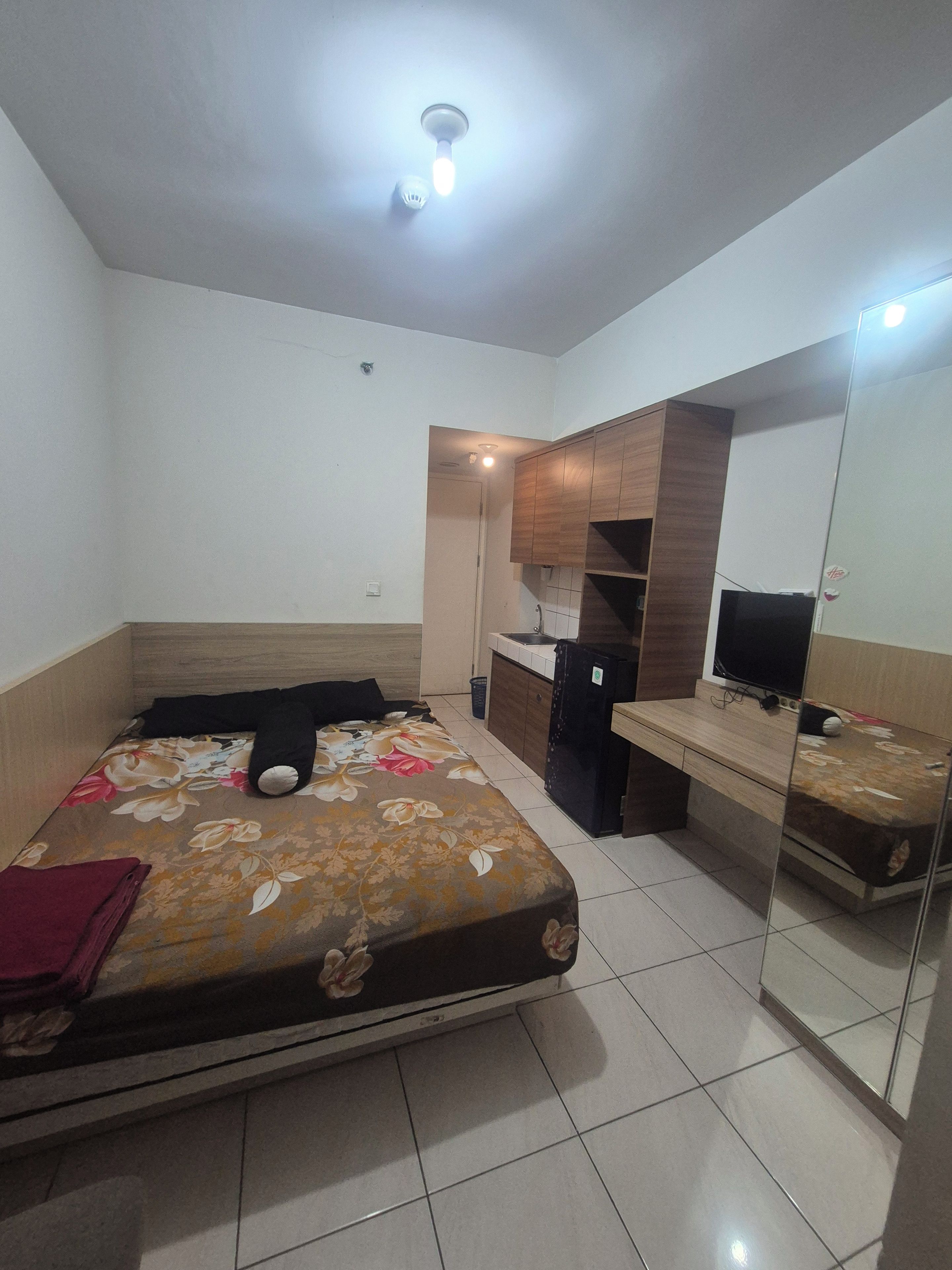 A bedroom with a bed, a desk, a mirror, and a ceiling light.