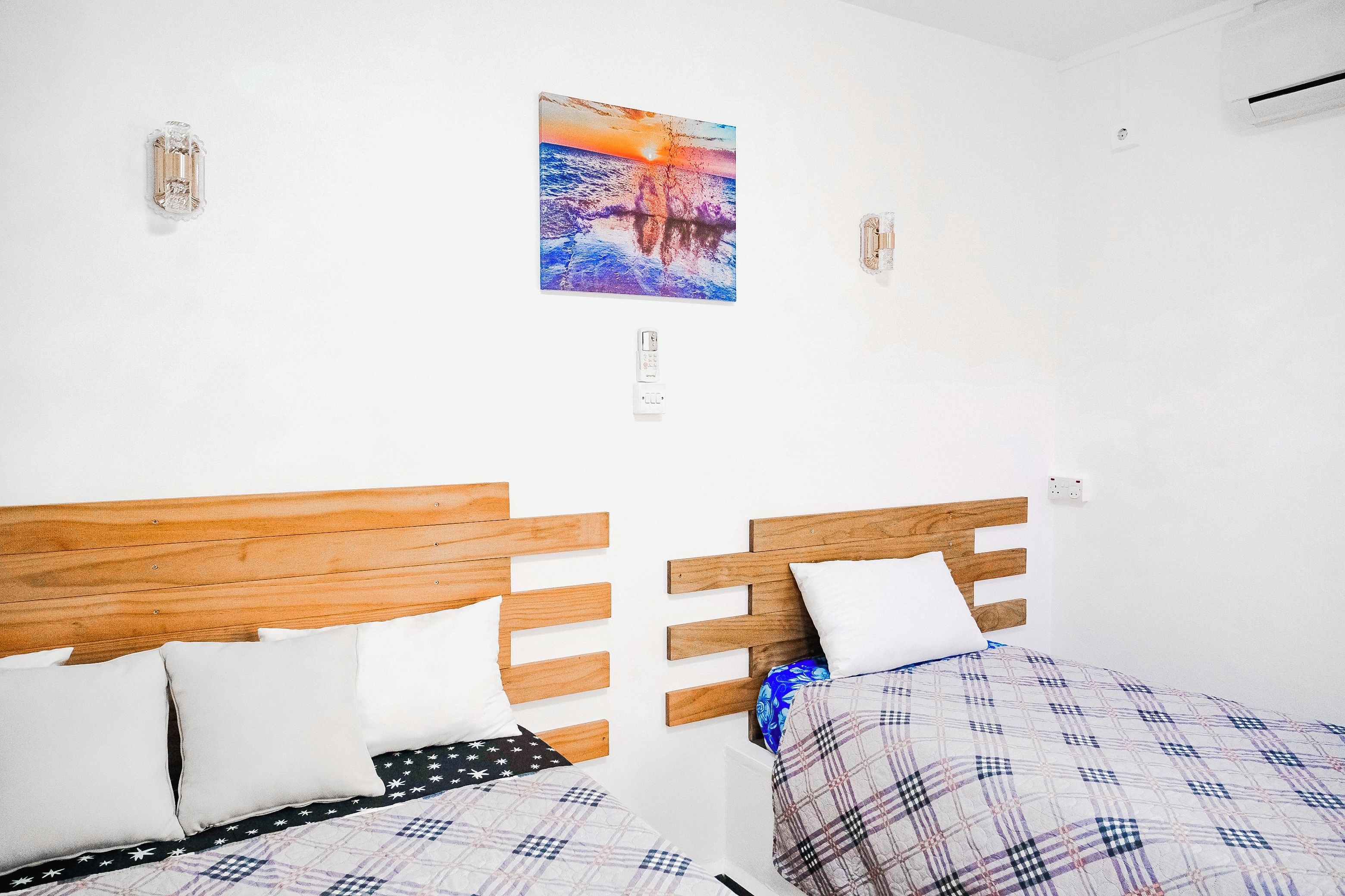 Ein Zimmer mit zwei Holzbetten, weißen Wänden und einem Sonnenuntergangsbild.