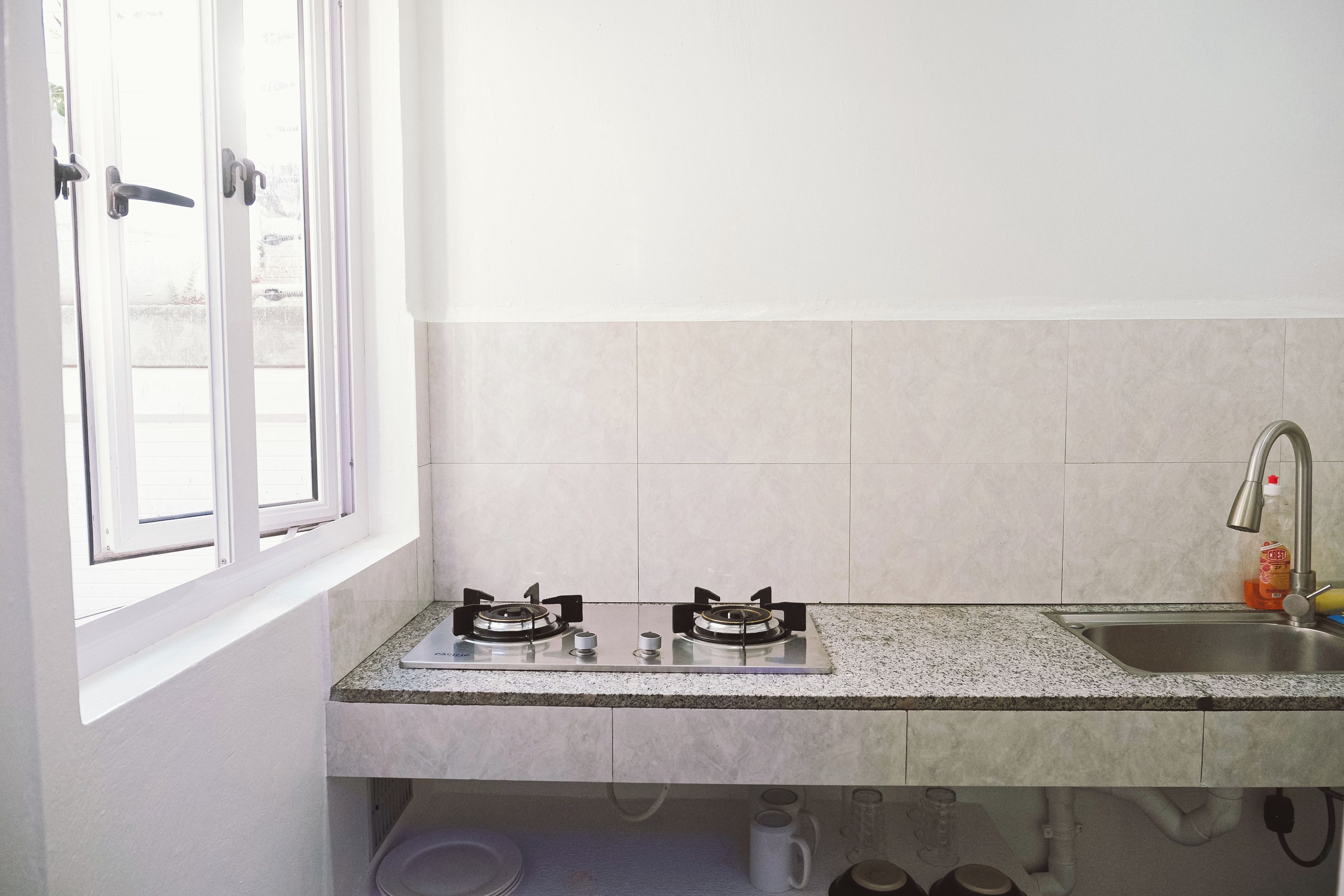 A kitchen with two gas stoves, a stainless steel sink, and a window with white frames.