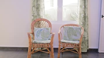 Two wicker chairs with leaf-patterned cushions in front of a window with curtains.