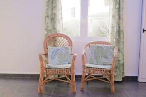 Two wicker chairs with leaf-patterned cushions in front of a window with curtains.