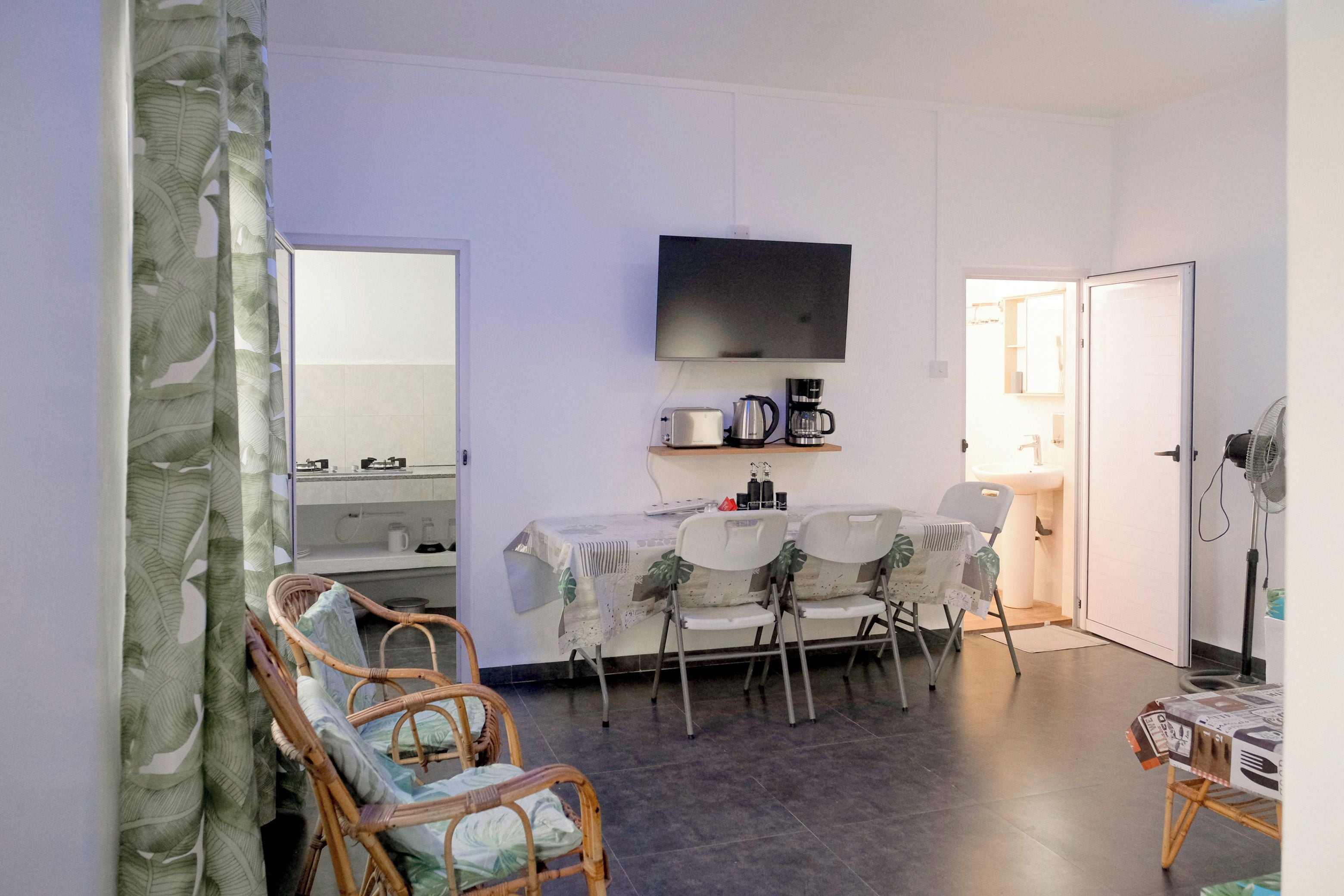 A compact living space with a dining area, a television mounted on the wall, and a kitchenette.
