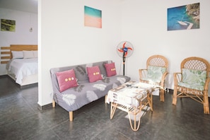 A modern room with a grey sofa, two wicker chairs, a small table, and a standing fan.