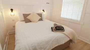 A bedroom with a large bed, two wall-mounted light fixtures, and a window with blinds.