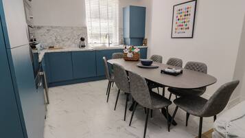 A modern kitchen with blue cabinets, a marble countertop, and a dining area with grey upholstered chairs.