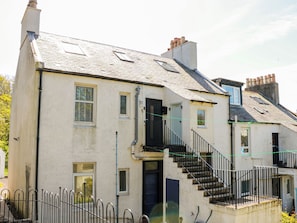 A two-story building with a staircase leading to the upper floor, a visible chimney, and a metal fence in the foreground. - Olea (Stranraer)