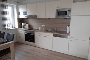 A modern kitchen with white cabinets, a stainless steel microwave, a built-in oven, and a coffee maker. - Holiday apartment with 2 bedrooms (Horumersiel)