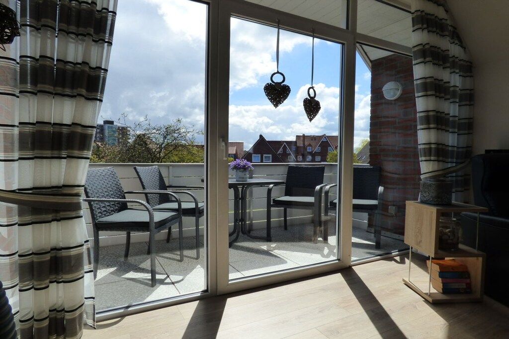 Un balcon avec une porte-fenêtre, une table, des chaises et une petite table d’appoint en bois sur laquelle sont posés des livres.