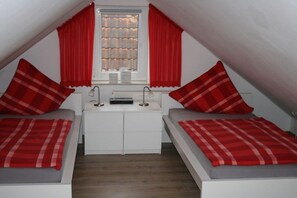 A small, triangular attic bedroom with two beds, a white dresser, and red curtains. - Holiday apartment with 2 bedrooms (Horumersiel)