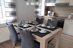 A modern kitchen with a dining area, featuring a wooden table, chairs, and a coffee maker. - Holiday apartment with 2 bedrooms (Horumersiel)