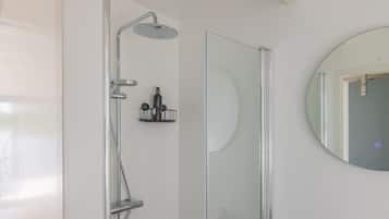 Un baño moderno con cabina de ducha de vidrio, un espejo redondo y un pequeño estante con artículos de aseo.