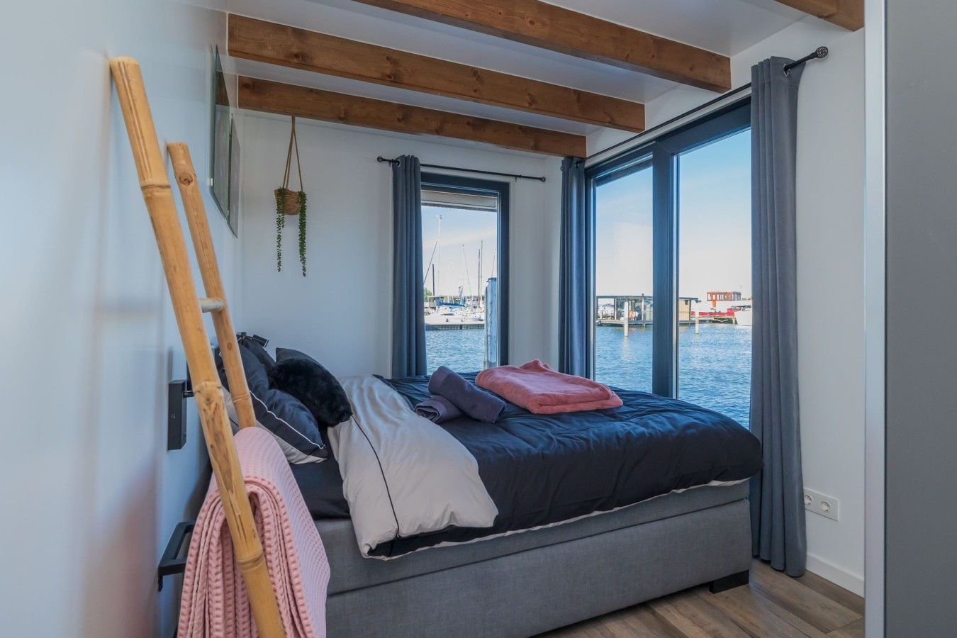 Un dormitorio con cama, ventana con vista al agua y techo de madera.