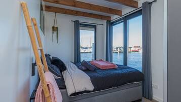 Un dormitorio con cama, ventana con vista al agua y techo de madera.