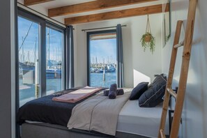 A bedroom with a bed, a window overlooking a marina, and a wooden ladder.