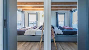 Een kamer met twee bedden, grote ramen, houten balken en uitzicht op een jachthaven.